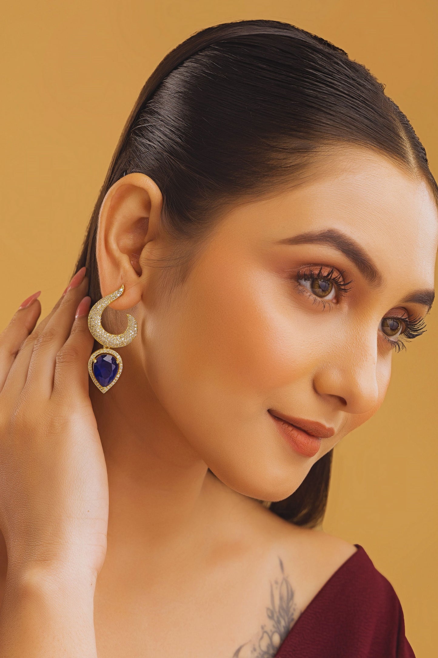 Woman wearing a gold and blue earring against a beige background