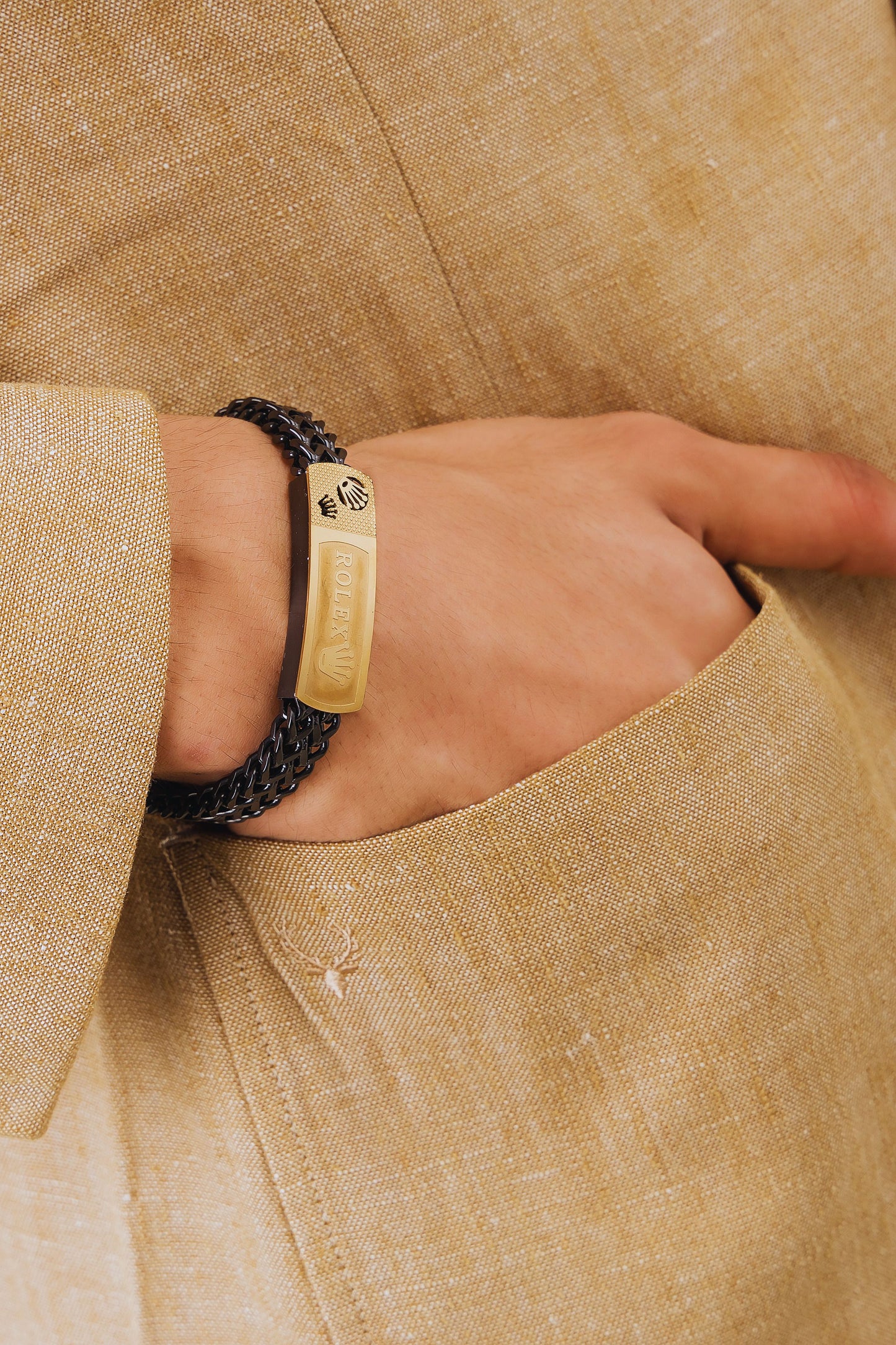 Close-up of a hand wearing a gold bracelet with a textured band, set against a beige fabric background.