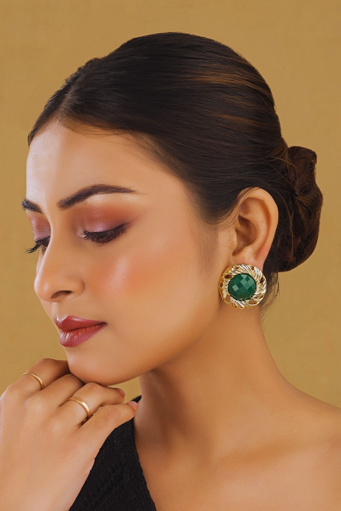 Woman wearing a gold earring with a green gemstone against a beige background