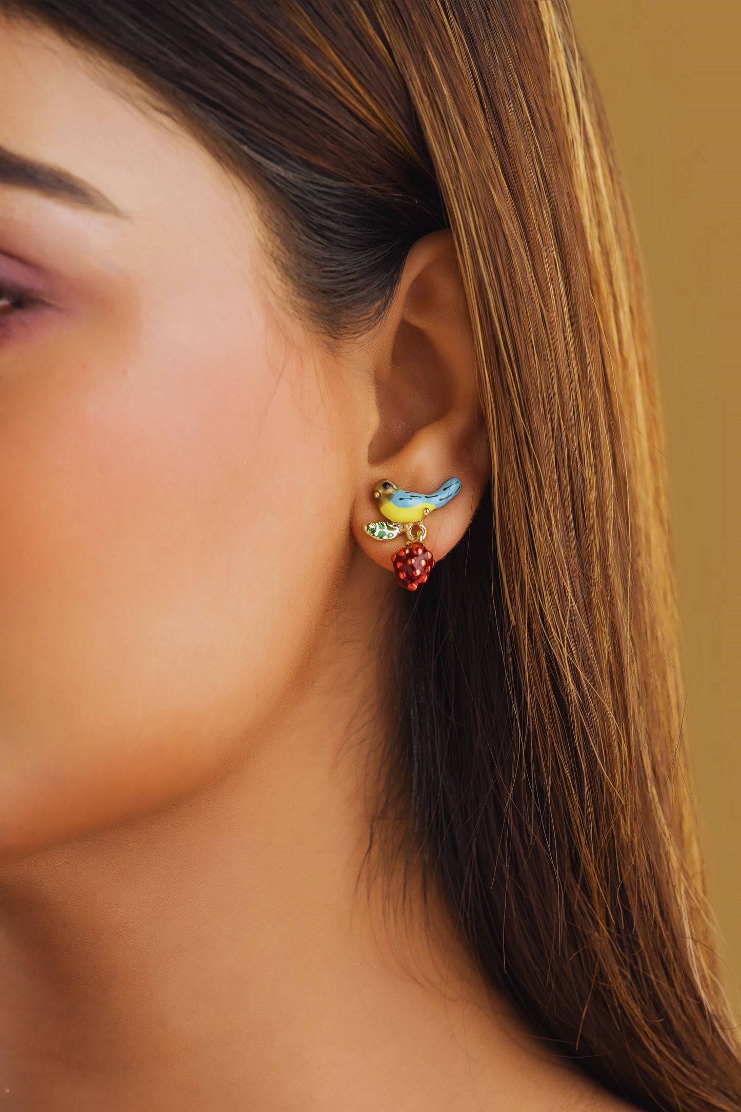 Close-up of an ear wearing colorful bird-shaped earrings against a neutral background
