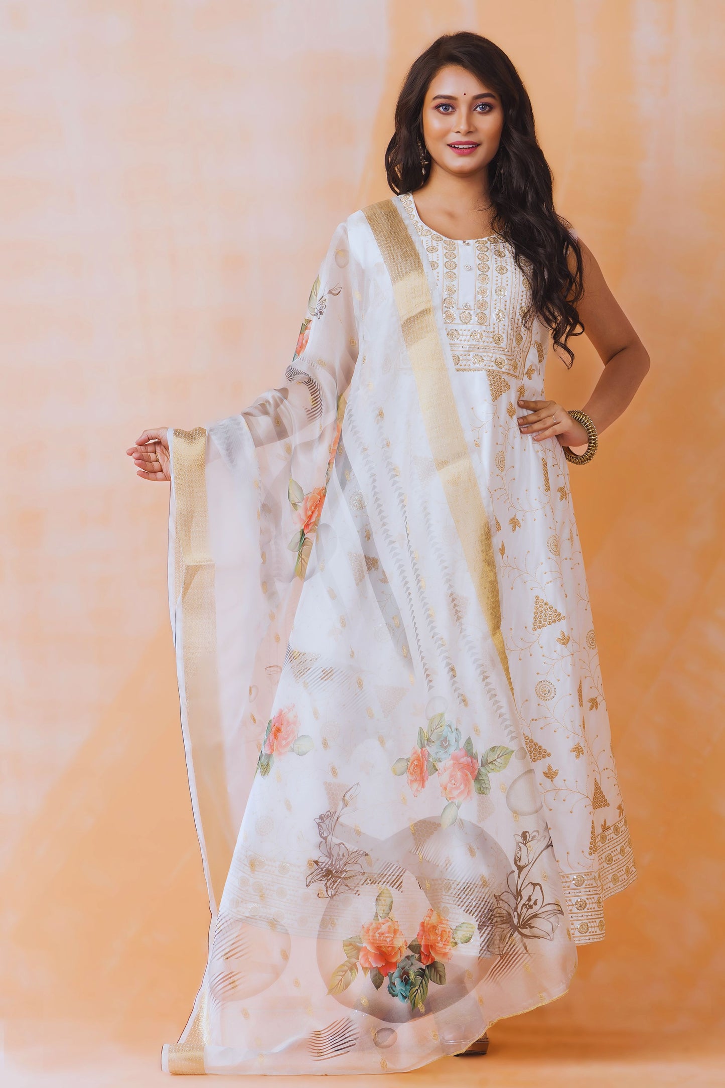 Woman wearing a white floral dress with a beige dupatta against an orange background