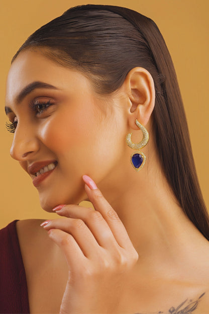 Woman wearing gold hoop earrings with a blue gemstone on a beige background