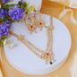 Gold and silver beaded jewelry set with red and green gemstone floral motifs, displayed on a white round pedestal with purple flowers and yellow satin fabric.