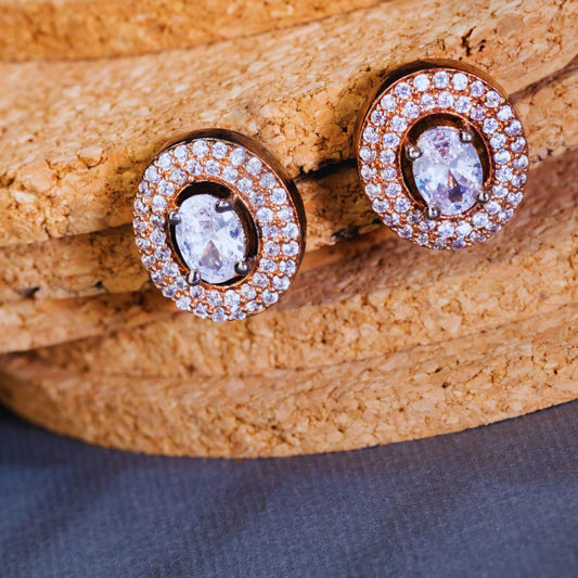 Pair of rose gold earrings with clear gemstones on a cork surface