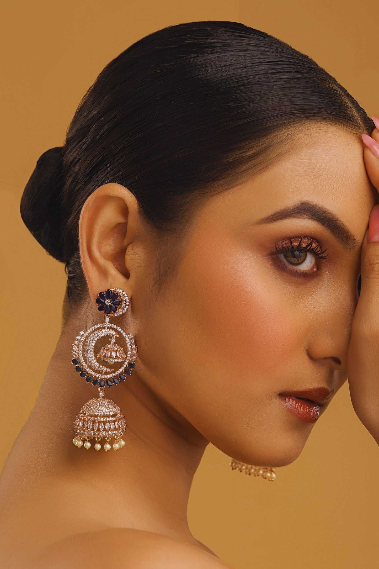 Woman wearing large, ornate earrings against a warm brown background