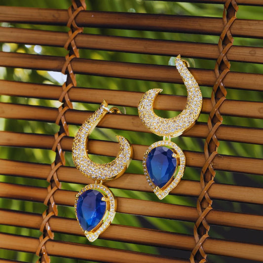 Gold earrings with blue gemstones on a woven surface