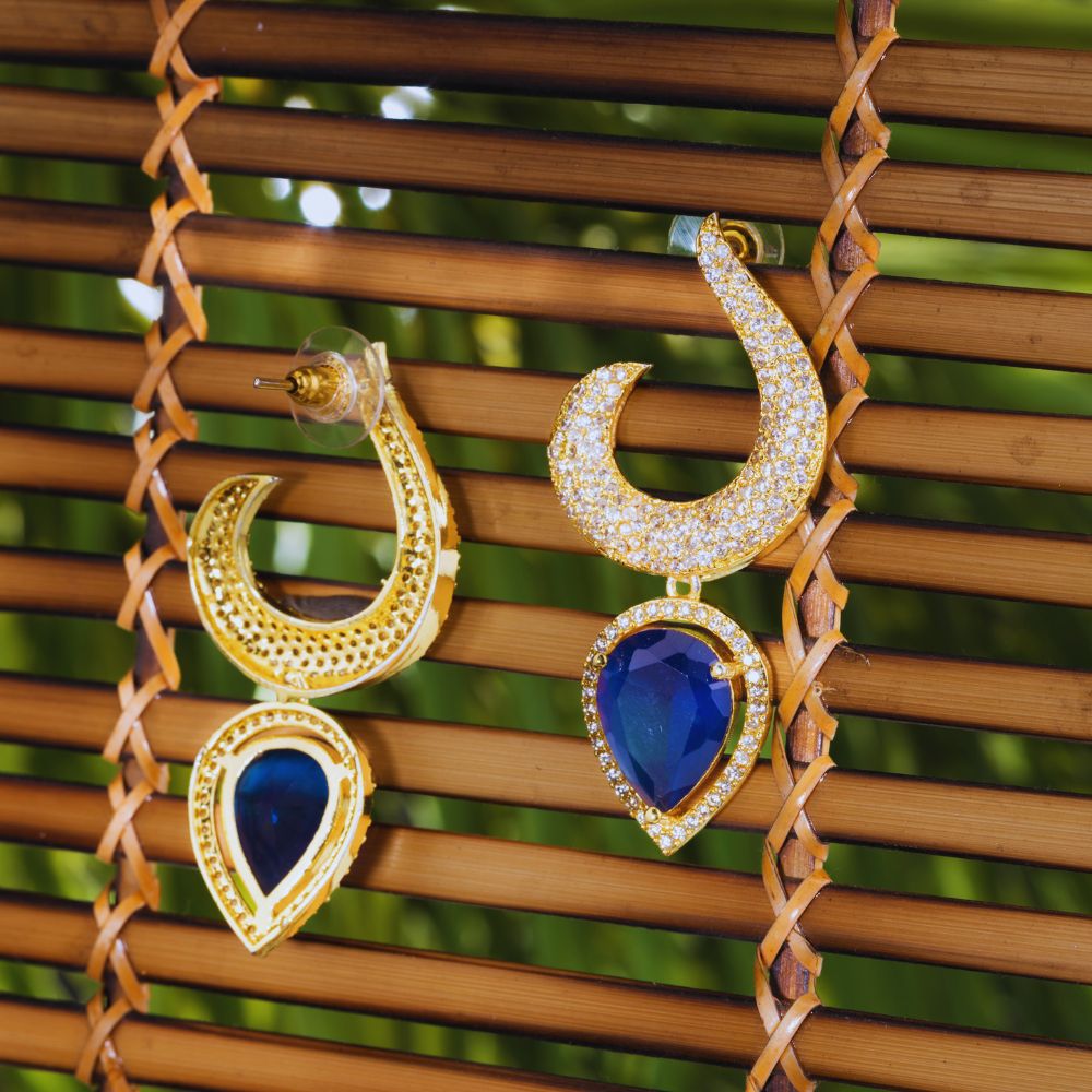 Gold and blue earrings hanging on a woven bamboo surface with a blurred green background