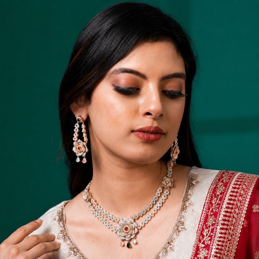 A woman wearing a traditional Indian jewelry set featuring a silver-toned necklace and matching earrings with gold and pink floral details, set against a solid dark green background.