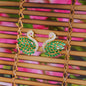 Peacock-shaped earrings with green gemstones on a woven surface with pink and green blurred background