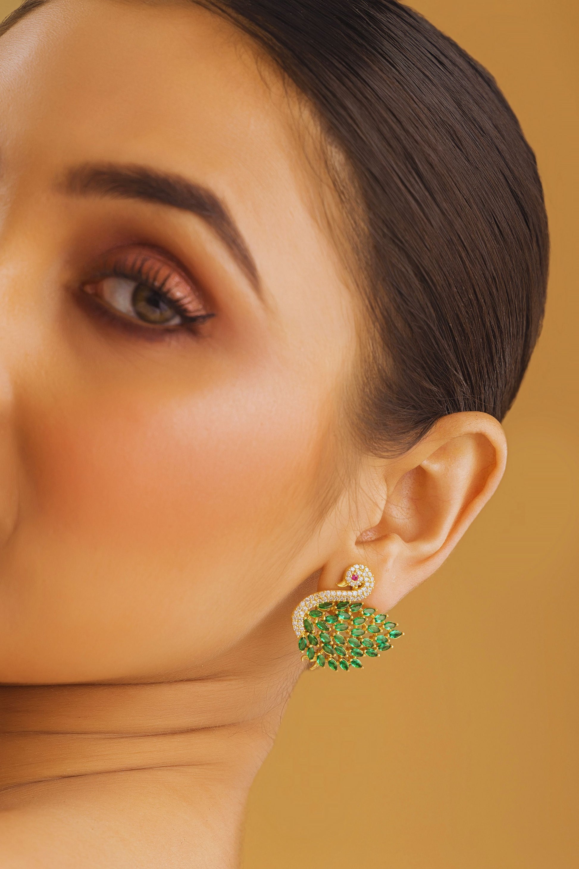 Close-up of a person wearing a green leaf-shaped earring against a beige background
