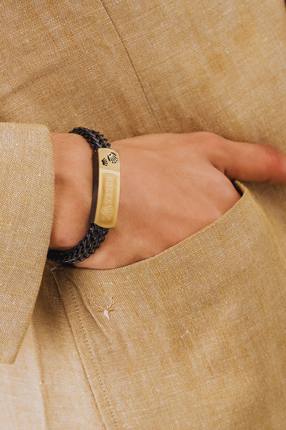 Close-up of a hand wearing a gold bracelet with a textured band, set against a beige fabric background.
