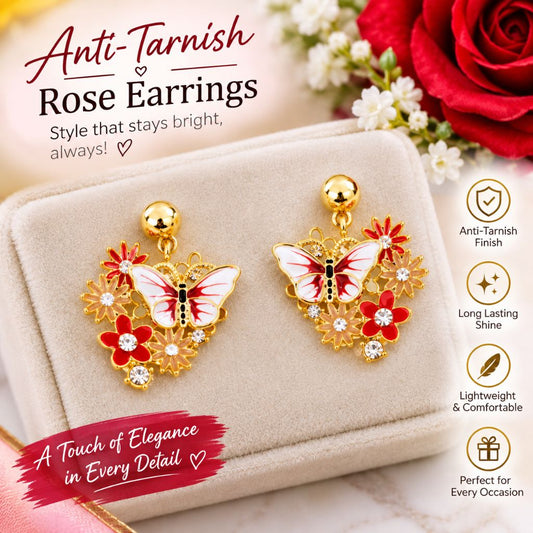 A pair of gold-tone rose earring charms displayed on a beige jewelry box. Each earring features a white and red butterfly with red flowers and small clear rhinestones.