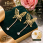 Gold butterfly drop earrings with rhinestone-studded chains, displayed on a dark green velvet jewelry box with a rose and promotional text from Tito's Fashion House.