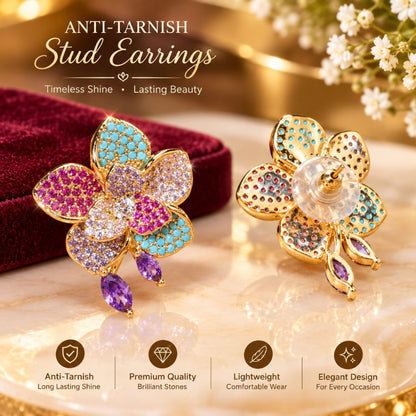 Two gold-tone stud earrings shaped like flowers, decorated with turquoise, pink, and purple rhinestones, displayed on a marble surface next to a dark red velvet box. The image includes promotional text at the top and feature icons at the bottom.