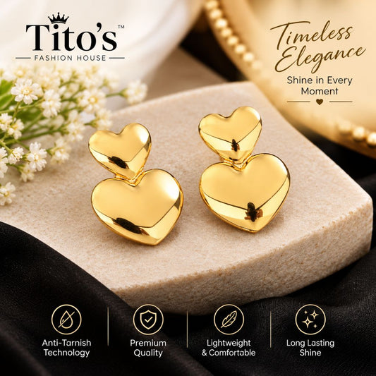 A pair of shiny gold heart-shaped stud earrings displayed on a beige stone block, with decorative white flowers and black fabric around them. The brand name 'Tito's Fashion House' appears at the top left, along with promotional text and feature icons at the bottom.