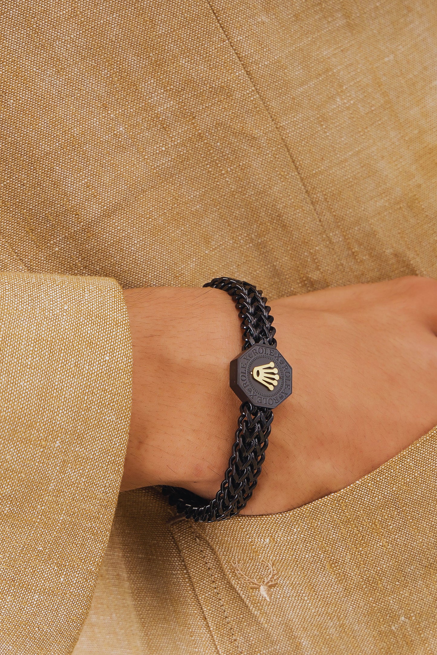 Black braided bracelet with a hexagonal emblem on a wrist against a beige fabric background
