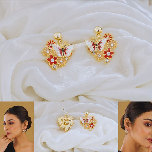 Butterfly-shaped earrings with floral details on a white fabric background, worn by a model.