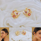Butterfly-shaped earrings with floral details on a white fabric background, worn by a model.