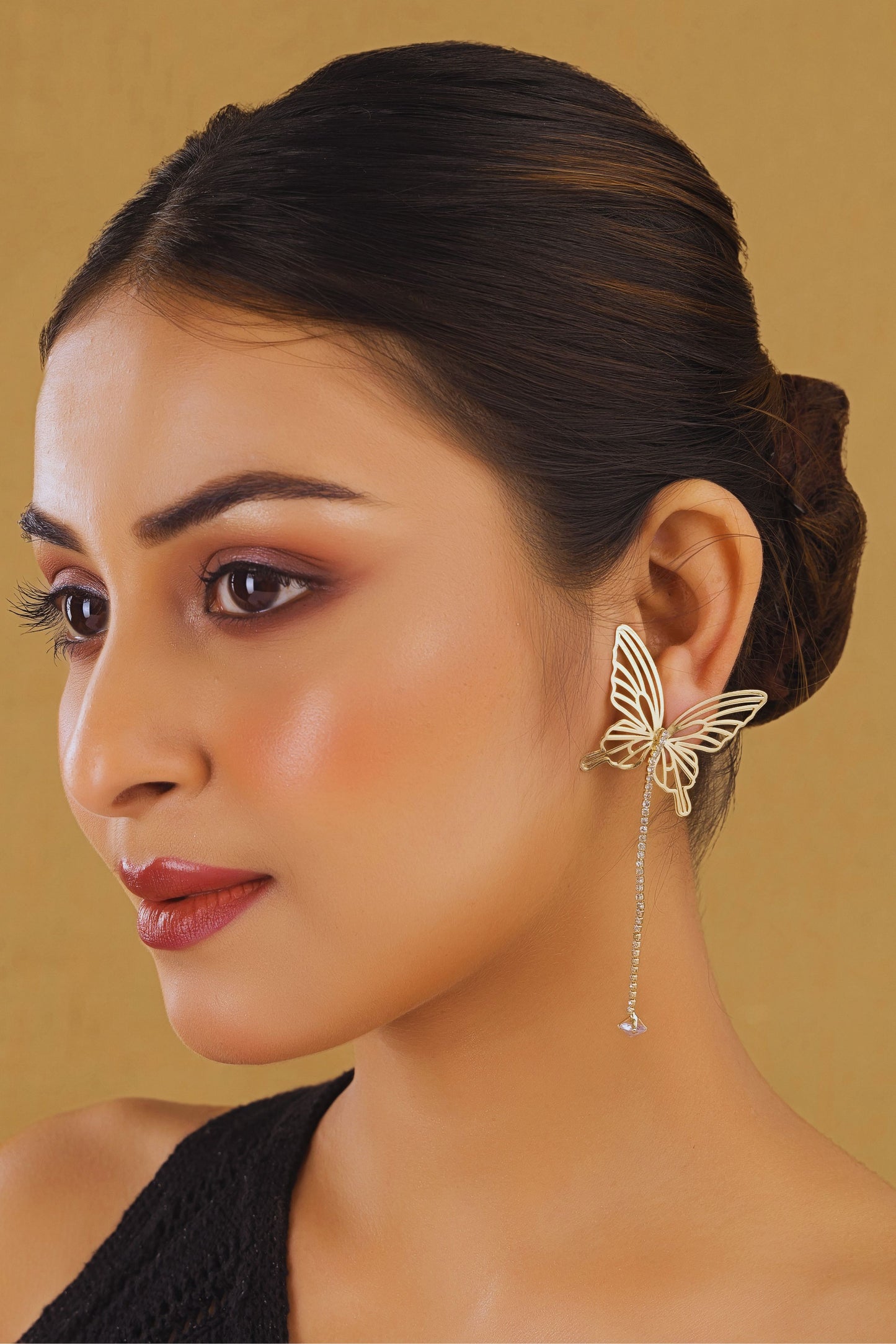 Woman wearing a butterfly-shaped earring against a beige background