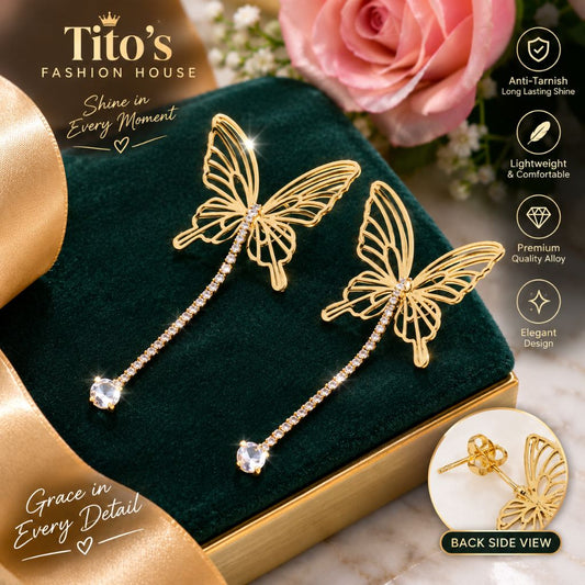 Gold butterfly drop earrings with rhinestone-studded chains, displayed on a dark green velvet jewelry box with a rose and promotional text from Tito's Fashion House.