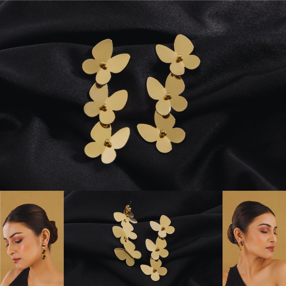 Gold butterfly-shaped earrings on a black fabric background with a model wearing them.