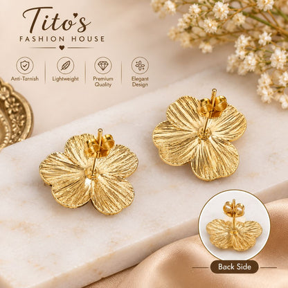 Two gold flower-shaped stud earrings displayed on a light marble surface, with a small inset showing the back side of one earring. The image includes marketing text and icons for anti-tarnish, lightweight, premium quality, and elegant design, along with decorative flowers and ribbon.