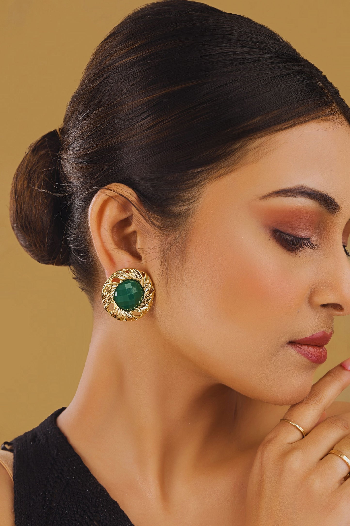 Woman wearing a gold earring with a green gemstone on a beige background