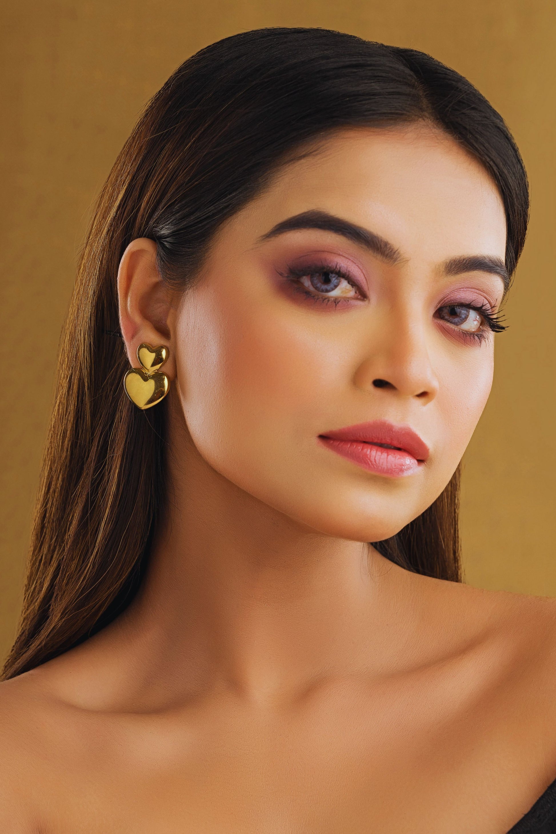 Woman wearing gold heart-shaped earrings against a beige background