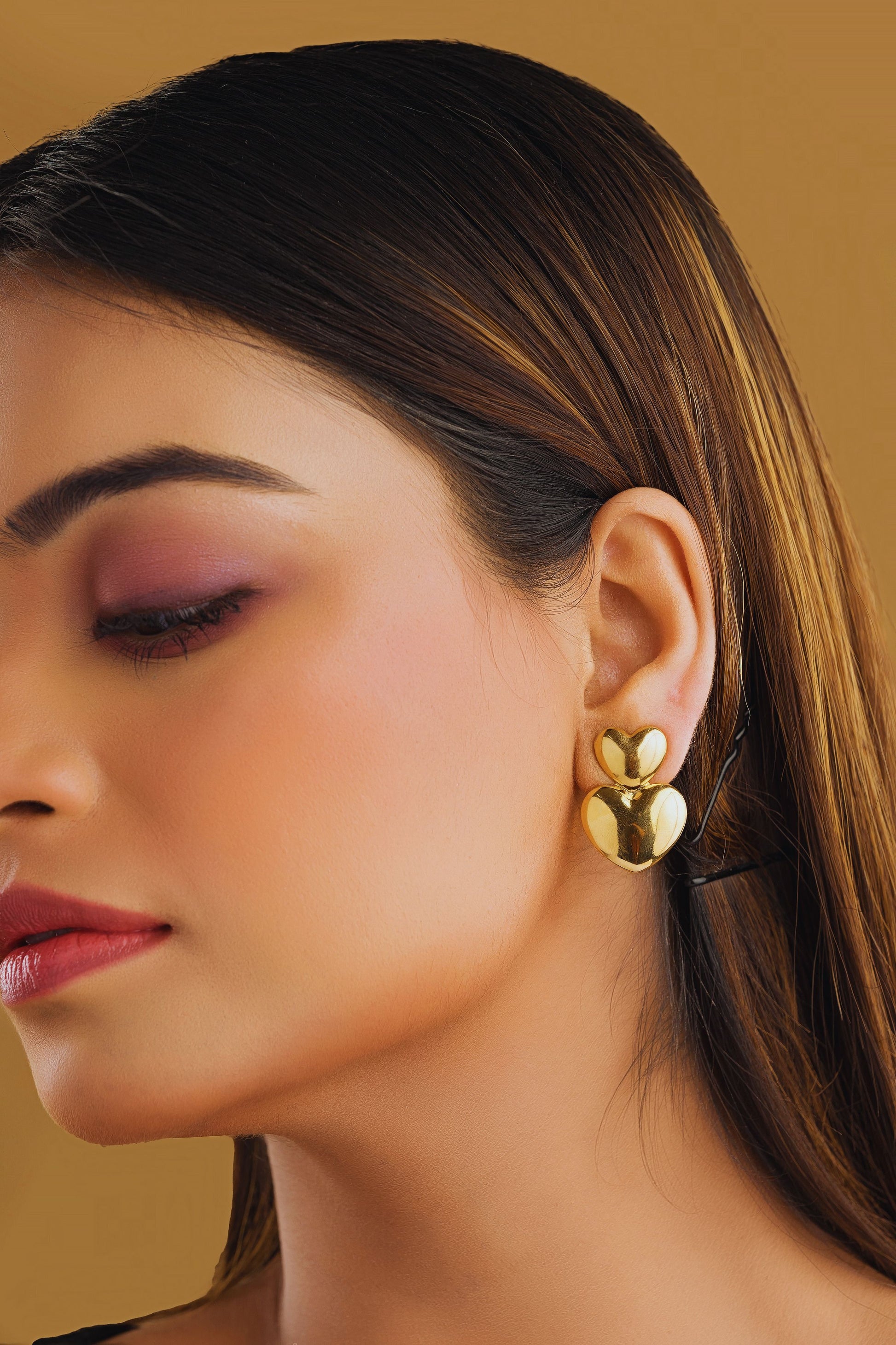 Close-up of a woman wearing gold earrings against a beige background
