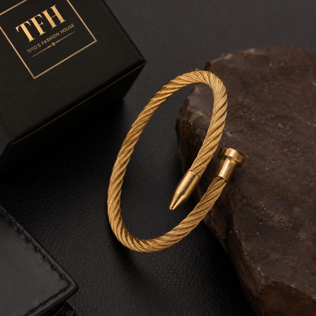 A gold-toned twisted rope cuff bracelet with a bullet-shaped tip, displayed on a dark textured surface next to a black branded box labeled TFH.