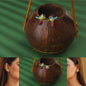 Bird-shaped earrings with red berries displayed on a coconut shell against a green background.