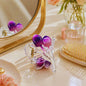 Purple hair clips on a vanity table with a mirror and hairbrush.