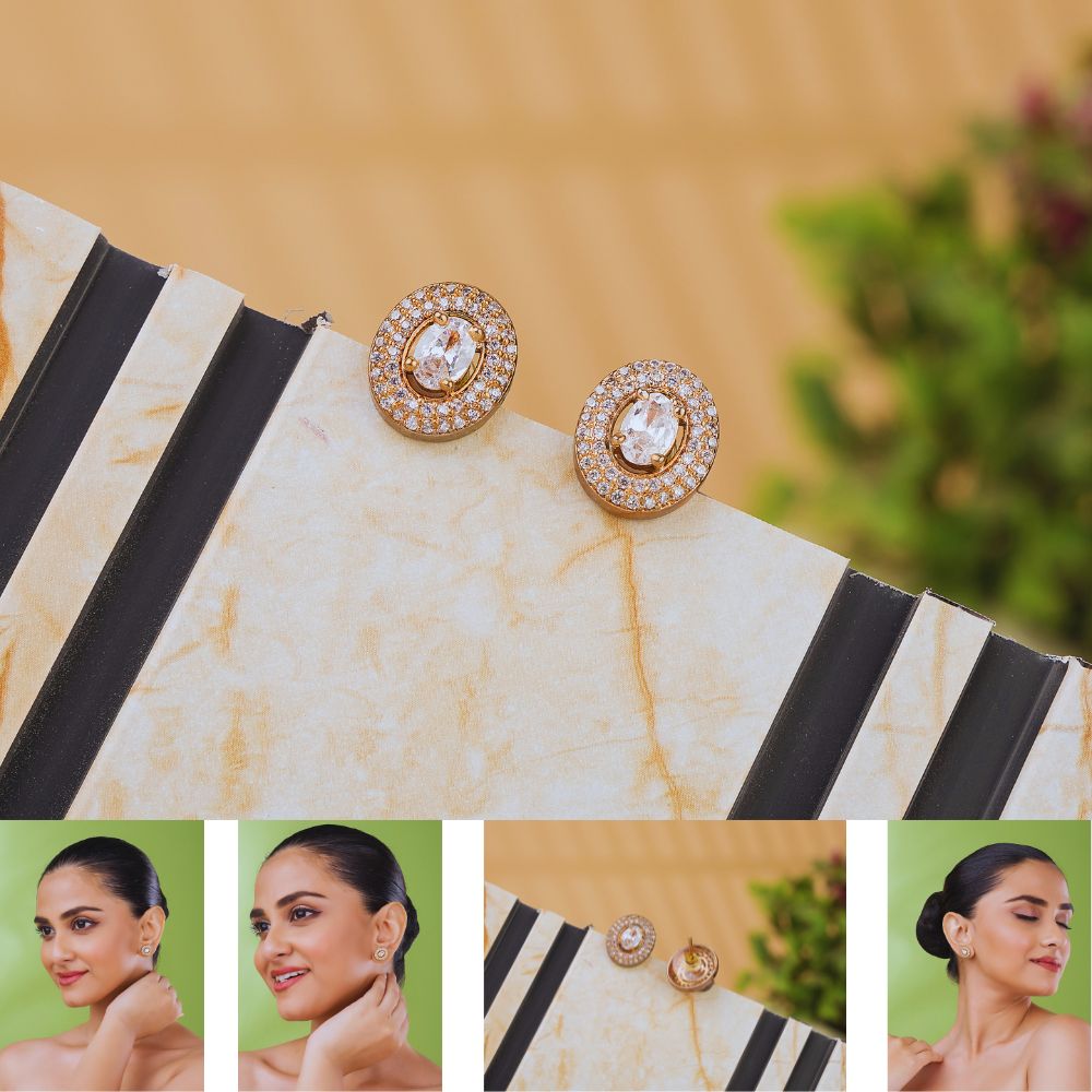 Gold earrings with clear stones on a marble surface, with a blurred green plant in the background.