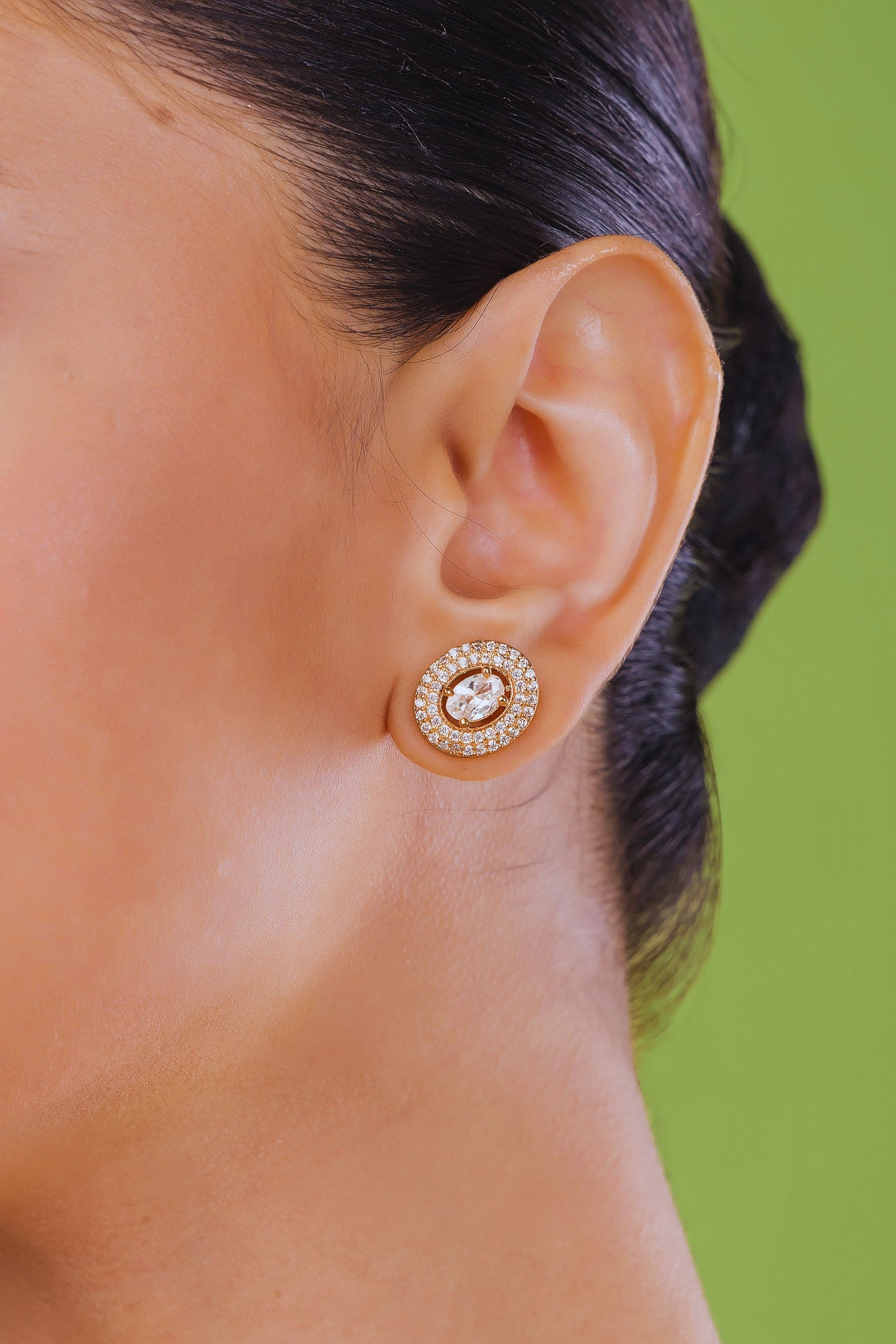 Close-up of an ear wearing a gold earring with a green background