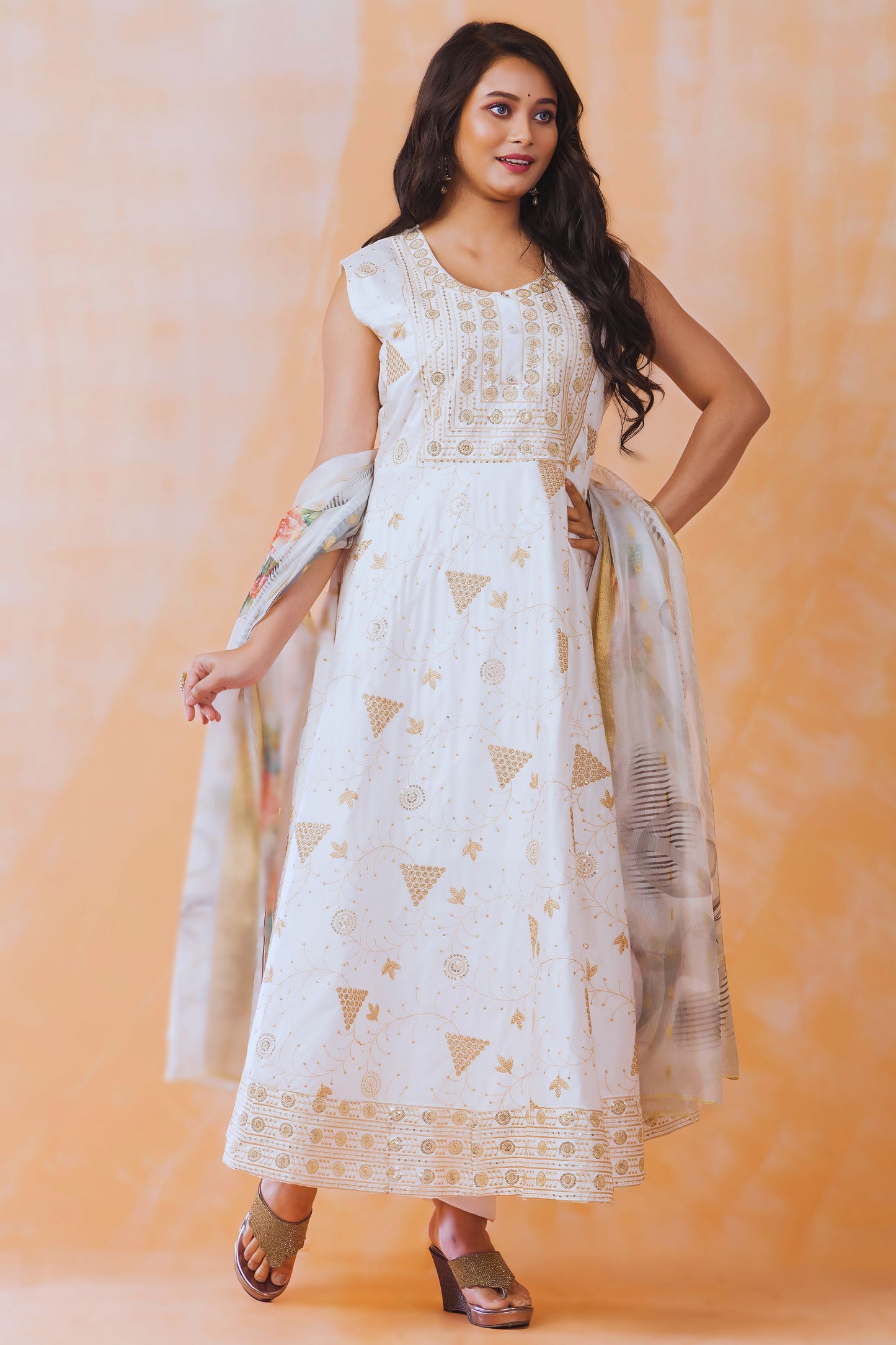 Woman wearing a white dress with gold patterns against an orange background