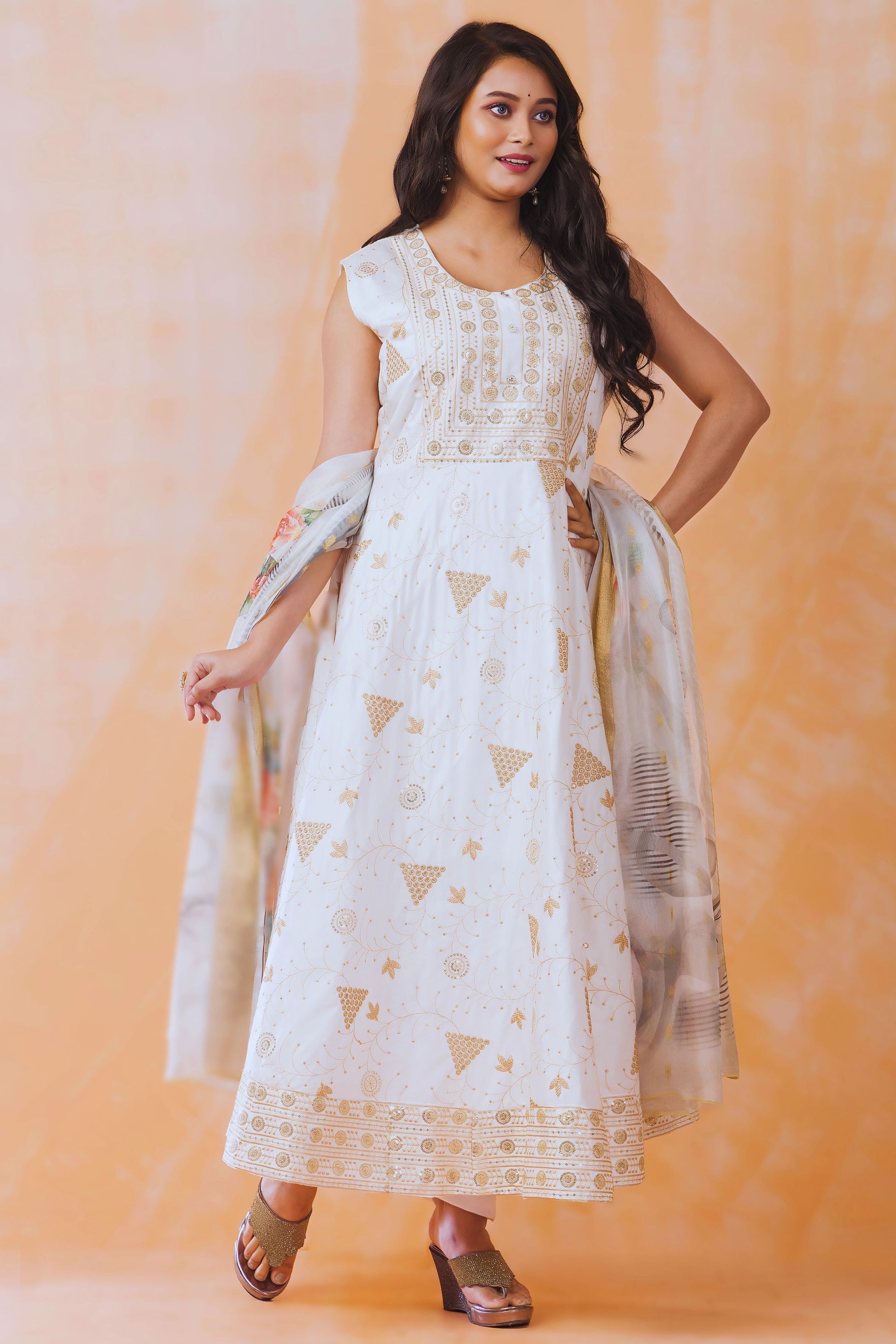 Woman wearing a white dress with gold patterns against an orange background
