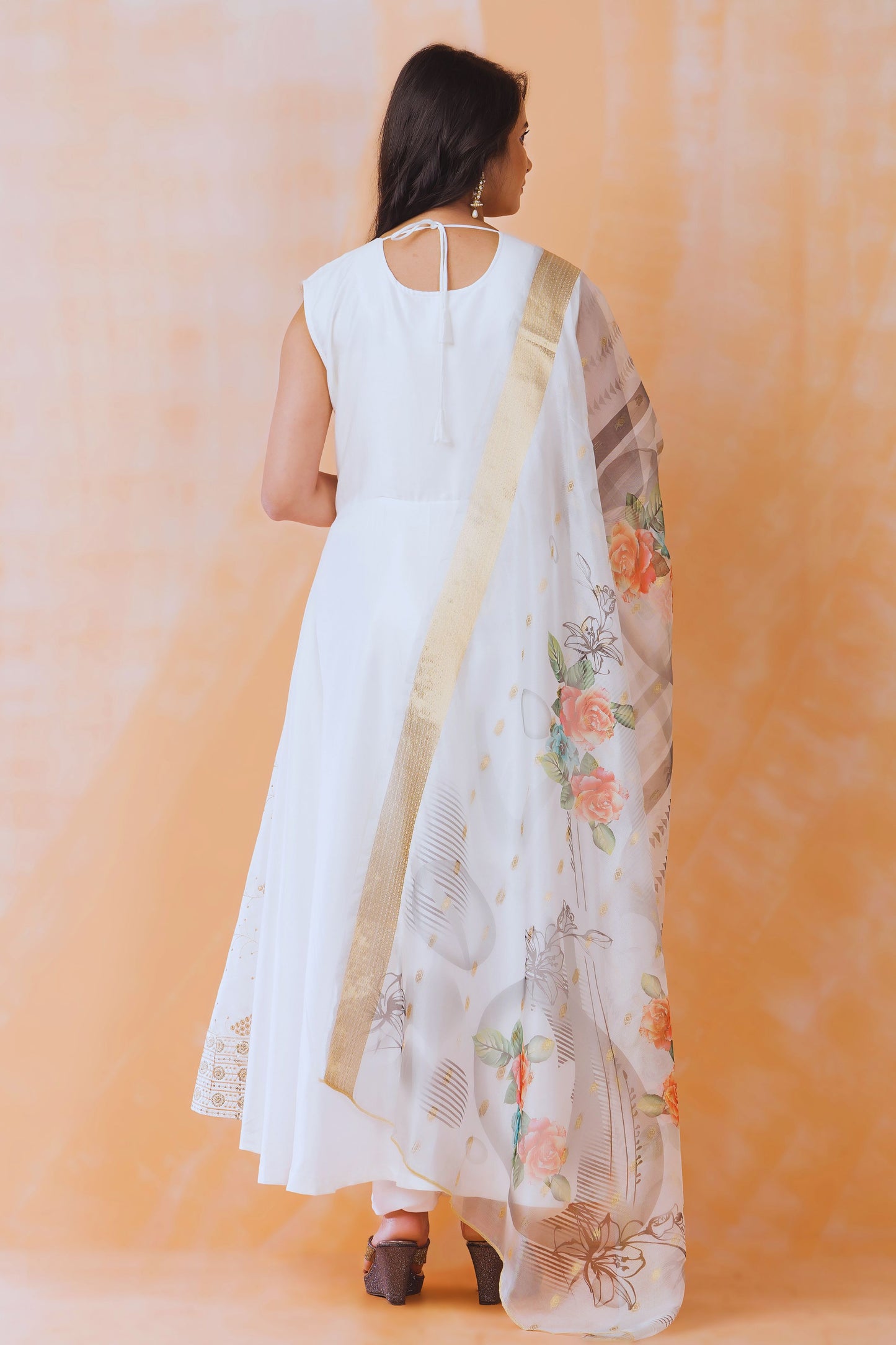 Woman wearing a white dress with a floral dupatta against an orange background