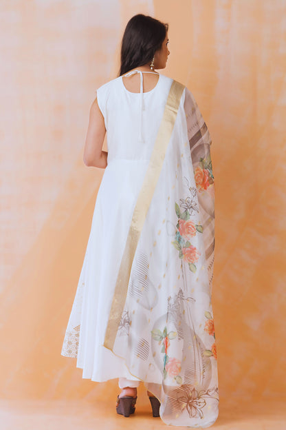 Woman wearing a white dress with a floral dupatta against an orange background