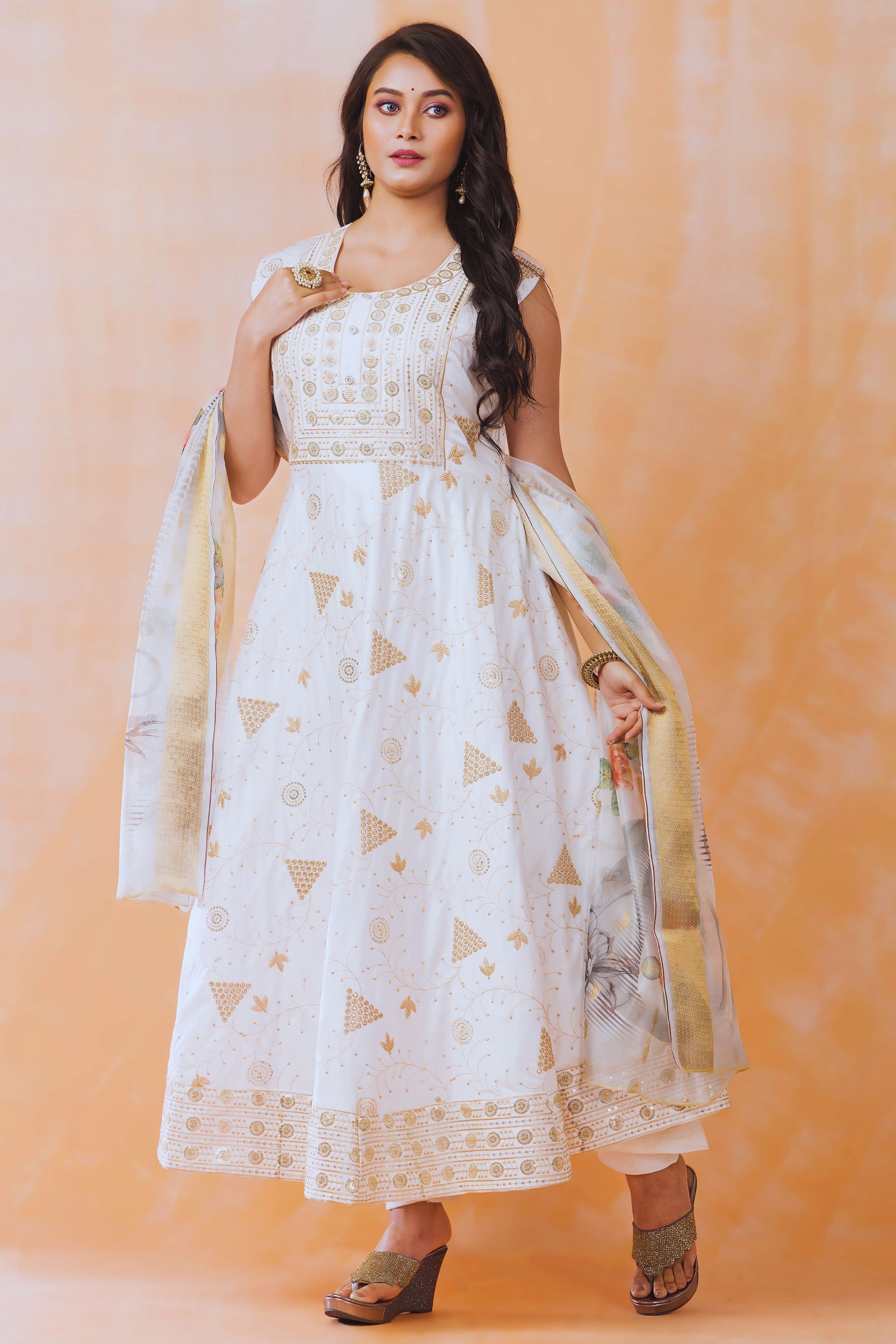 Woman wearing a white and gold traditional outfit with a dupatta against an orange background