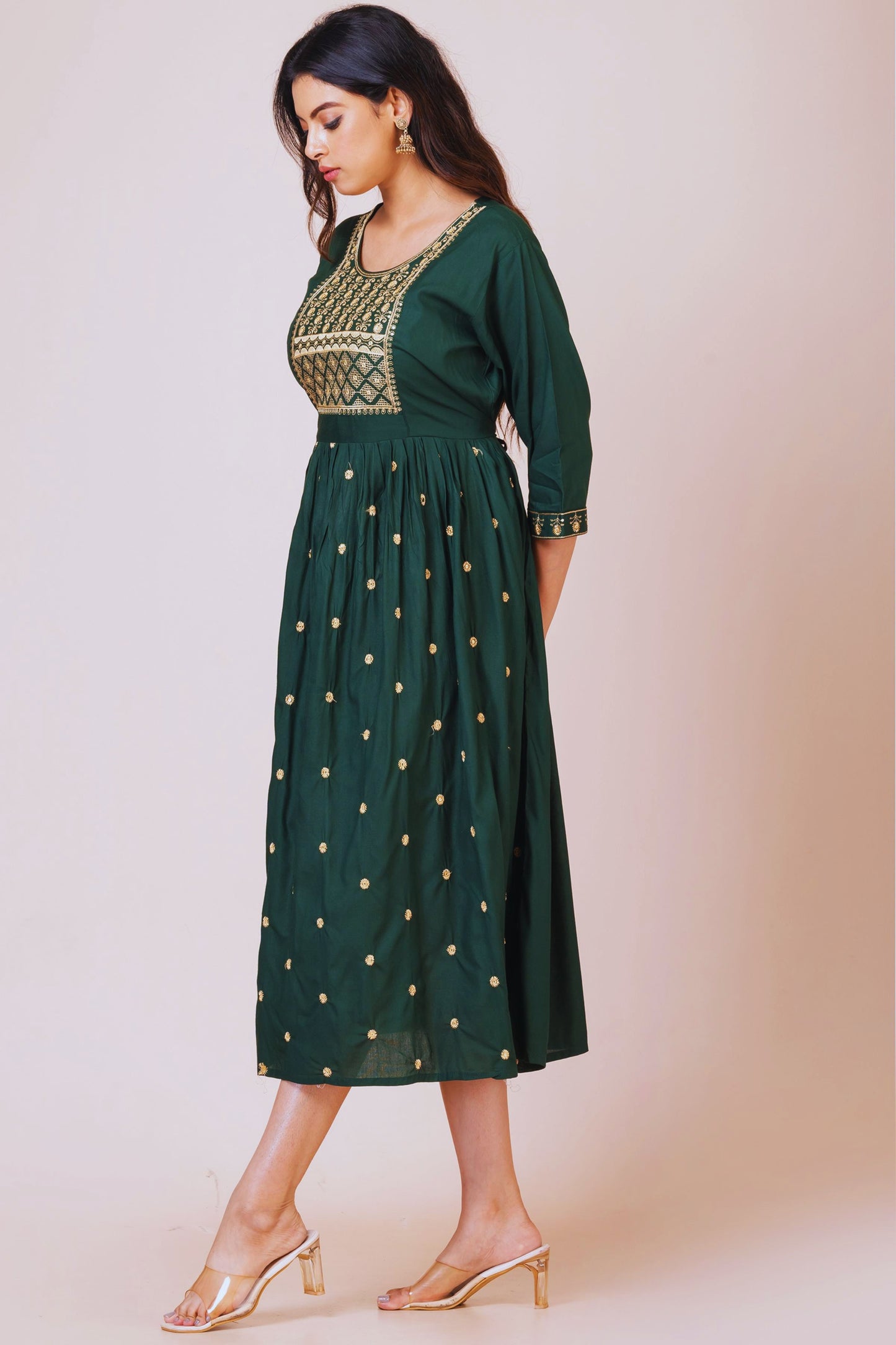 Woman wearing a green dress with gold embroidery against a beige background