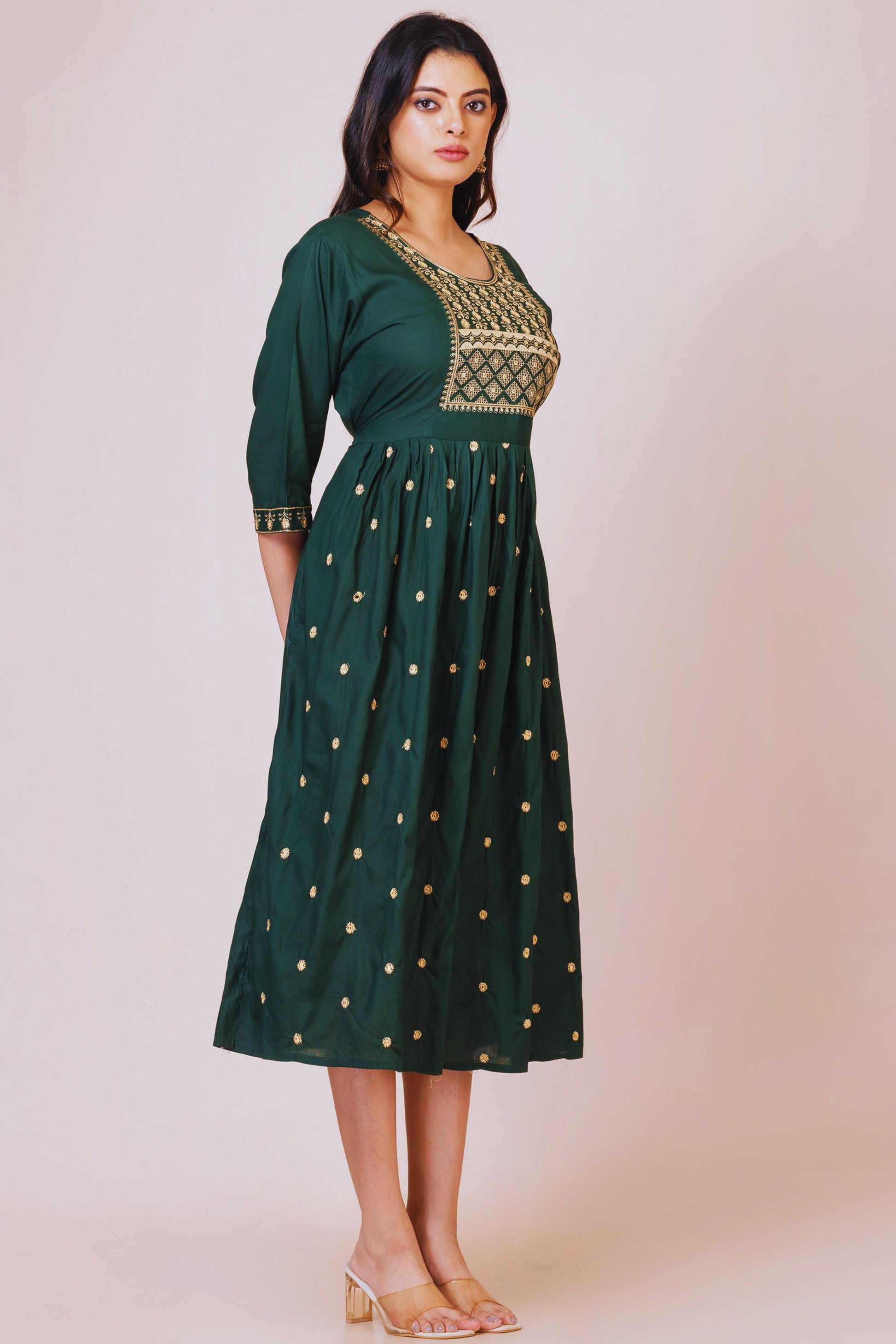 Woman wearing a green dress with gold embroidery on a beige background