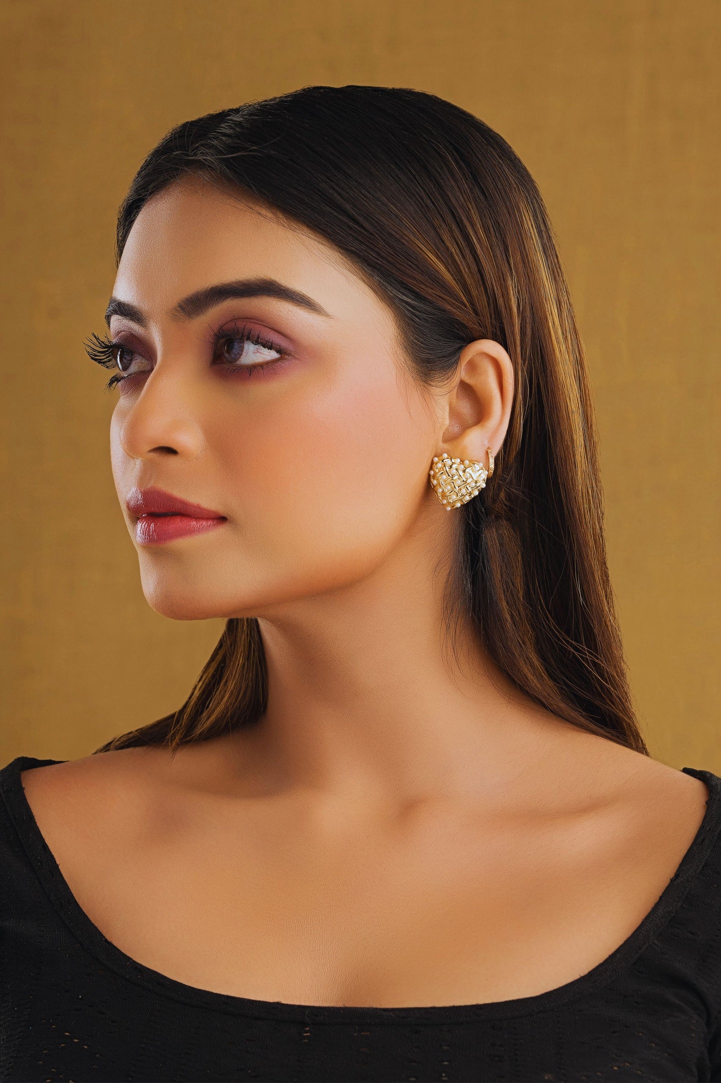 Woman wearing gold earrings against a beige background