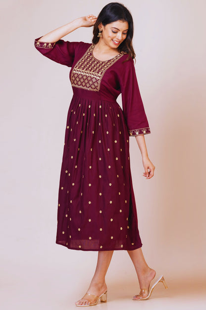 Woman wearing a maroon dress with gold embroidery on a beige background