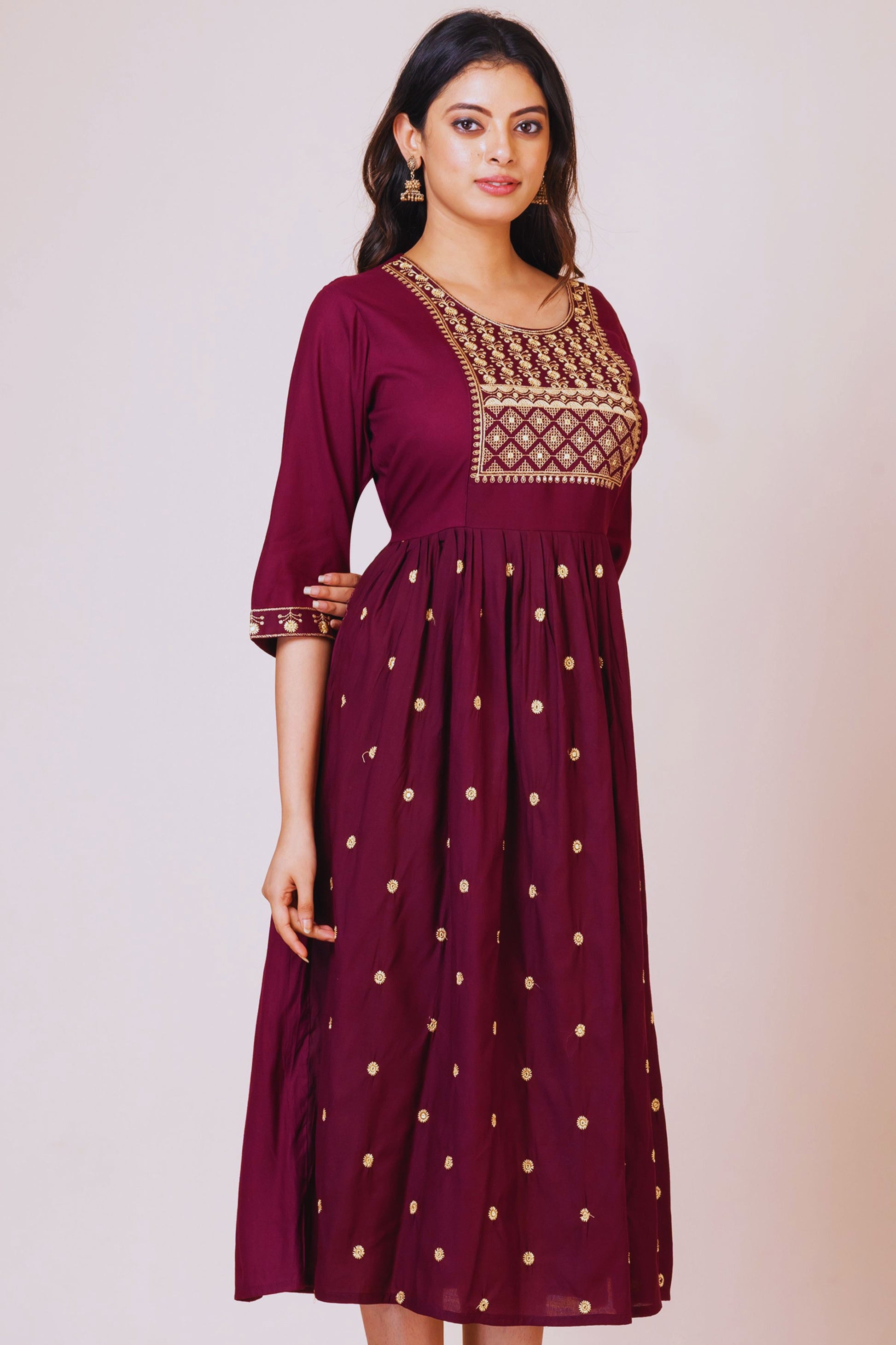 Woman wearing a maroon dress with gold embroidery on a plain background
