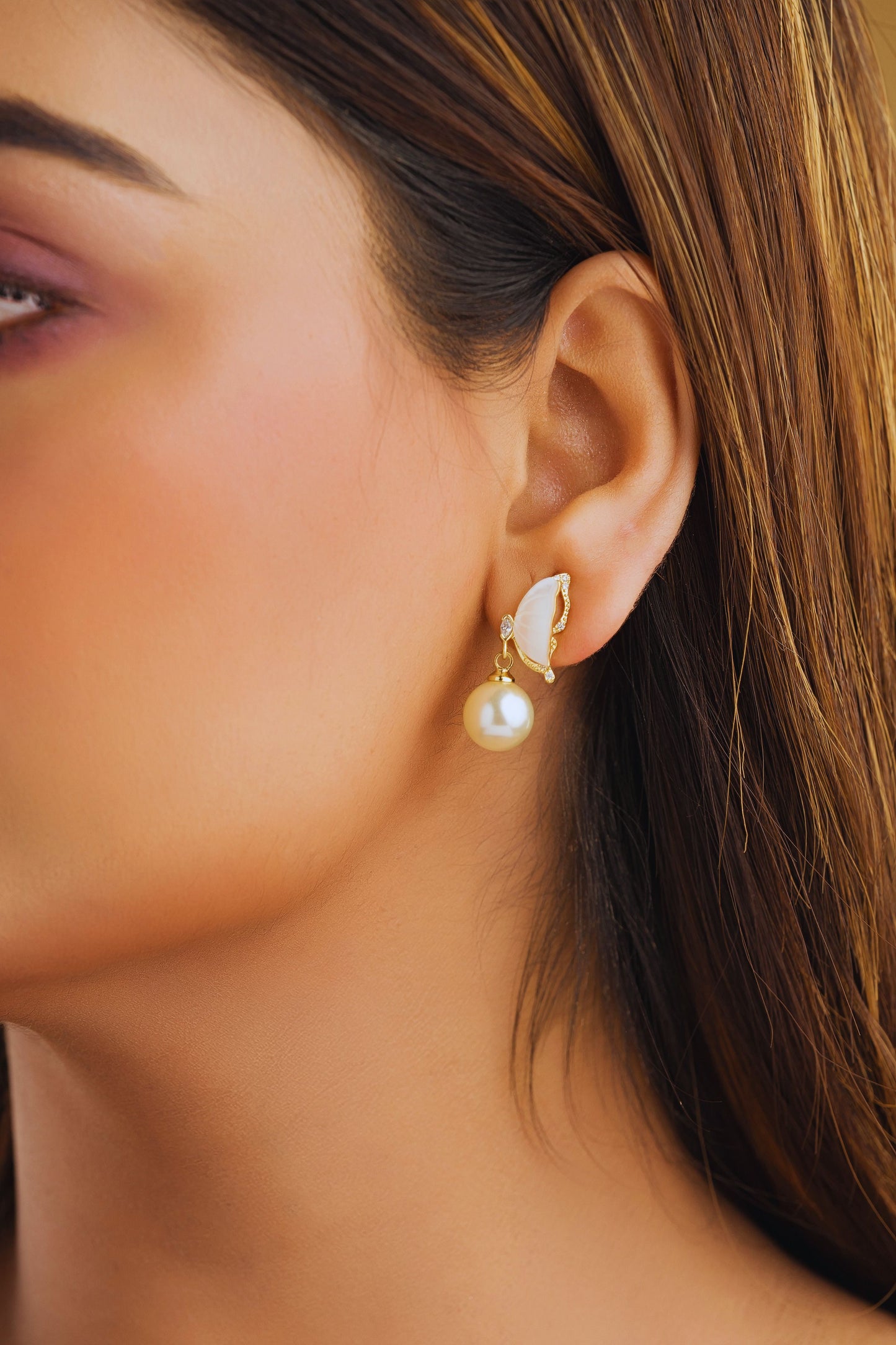 Close-up of a woman's ear wearing a pearl earring with a butterfly charm.