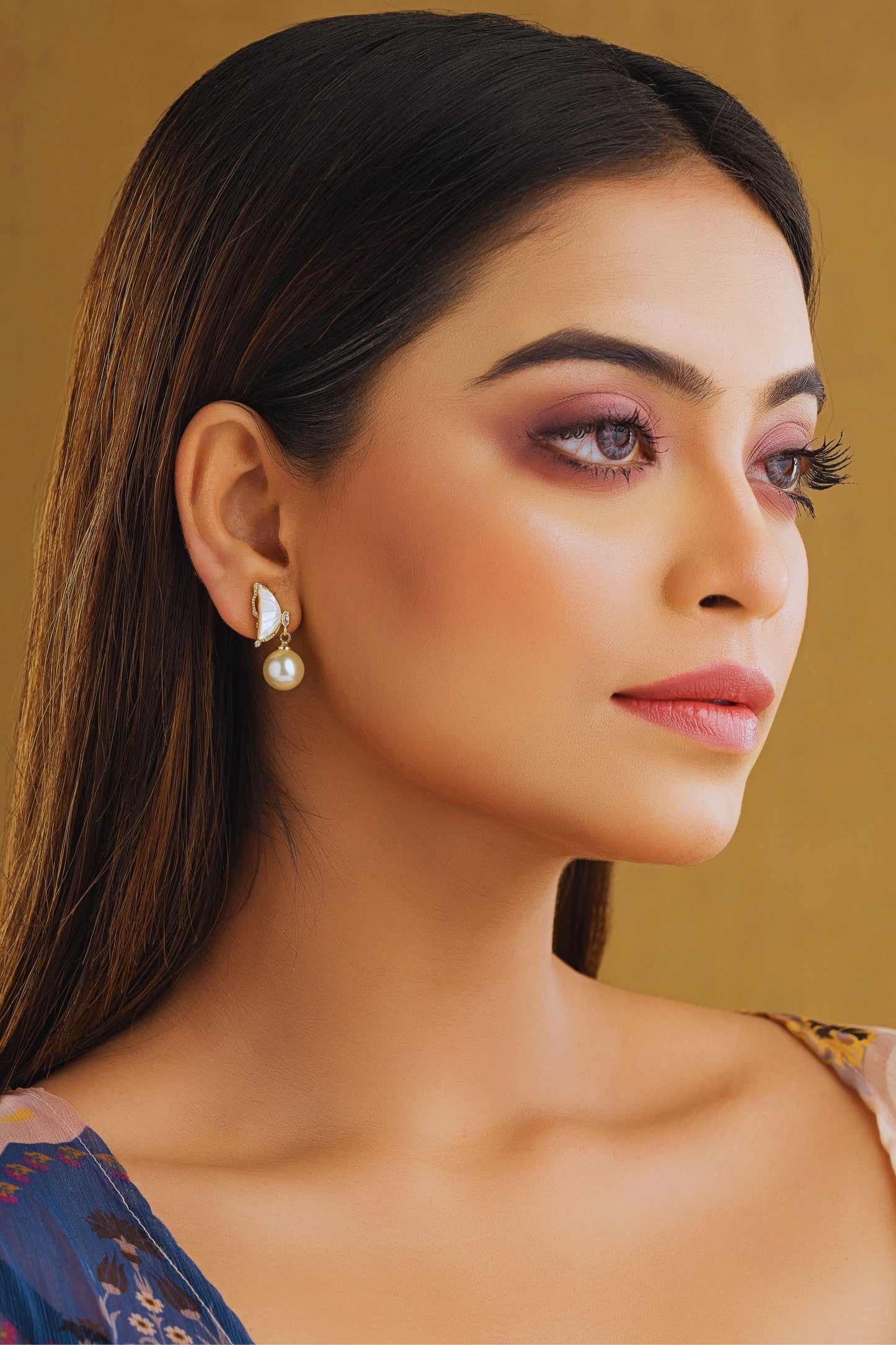 Woman wearing pearl earrings against a gold background