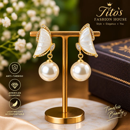 A pair of gold and mother-of-pearl butterfly drop earrings displayed on a gold stand, with a dark box, white flowers, and decorative text overlays in the background.