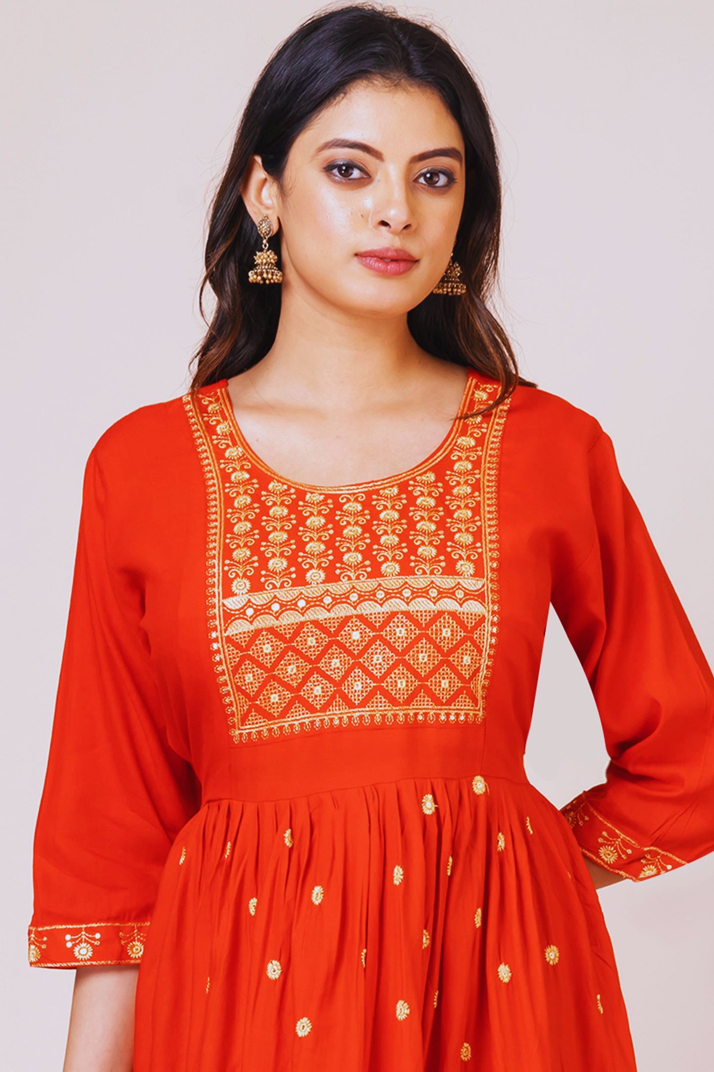 Woman wearing a red dress with intricate white embroidery on a plain background