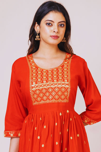 Woman wearing a red dress with intricate white embroidery on a plain background