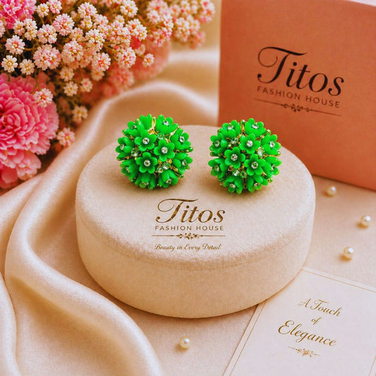 Green earrings on a 'Titos Fashion House' branded box with pink flowers in the background.